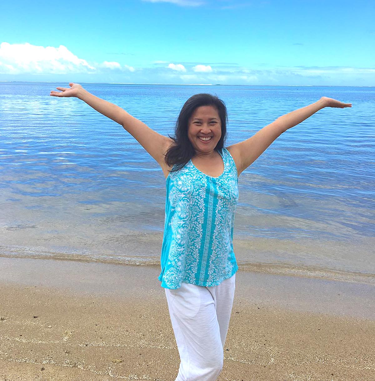 Amy Lang standing with her arms out on the beach.