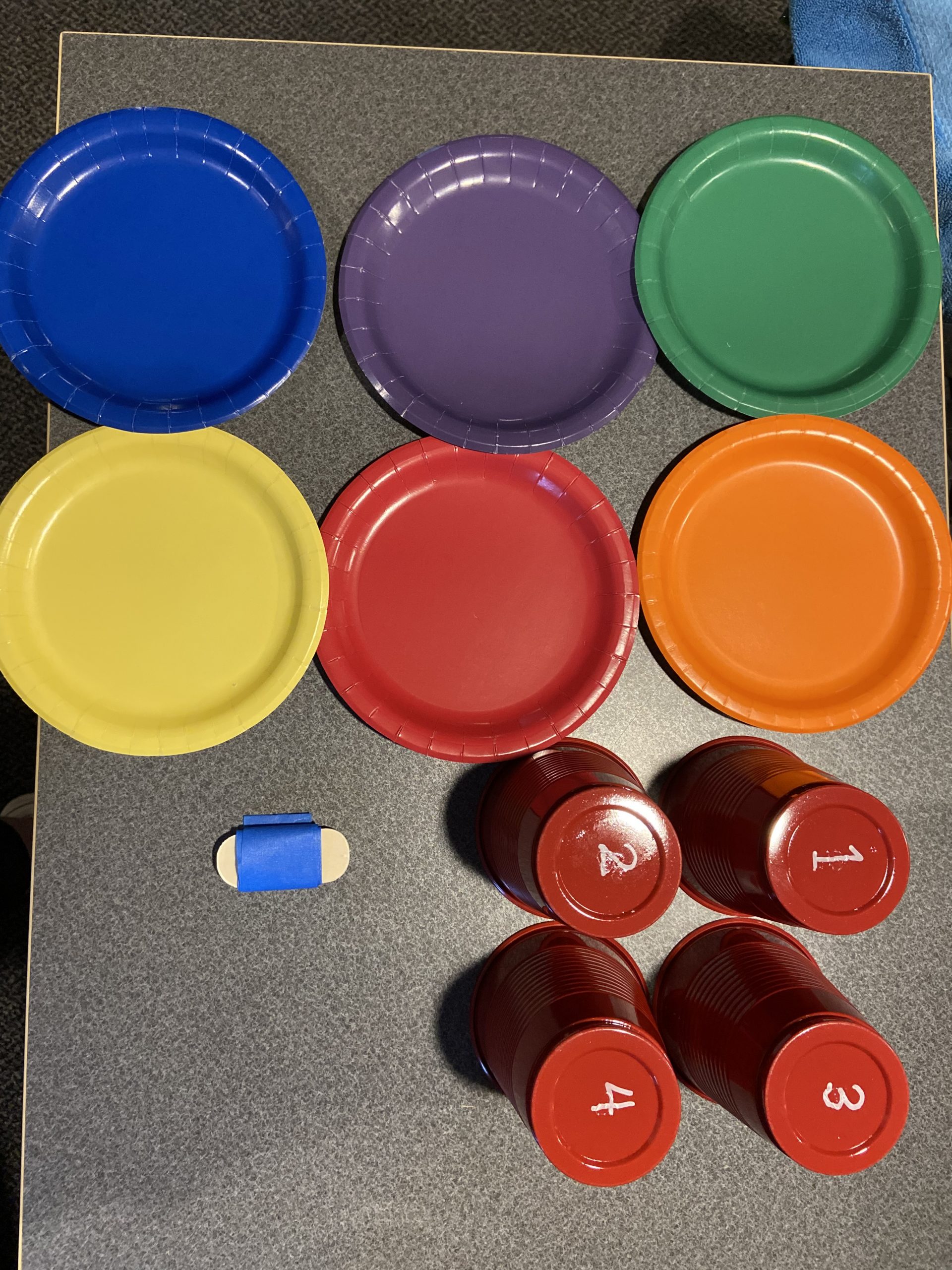 Photo of the supplies needed for the Balance and Brains virtual programming - colored paper plates, cups with numbers and blue painters tape