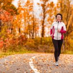 a woman in a track suit runs outdoors surrounded by fall foilage