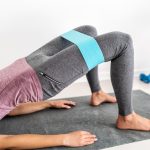 a woman wearing a resistance band demonstrates a glute bridge exercise on a mat