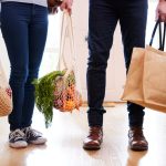 two people seen from the waist down, holding bags of groceries