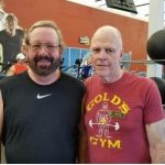 Two smiling men stand next to each other in a gym