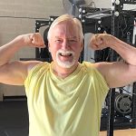 a white haired man in a yellow shirt flexes his arm muscles