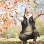 a smiling woman throws autumn leaves in the air