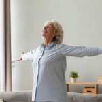 a woman stands with arms outstretched, eyes closed, smiling