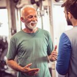 Older man speaking with younger man inside a gym