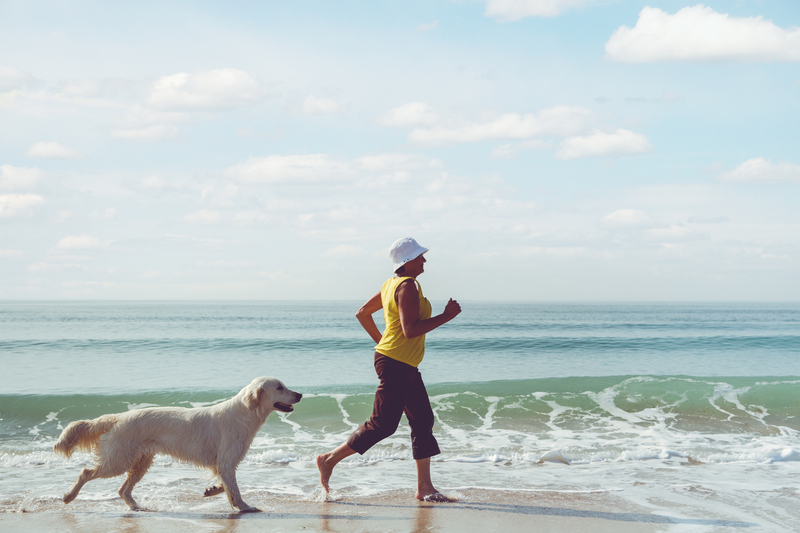 Middle aged woman running on beach with a dog (yellow lab)