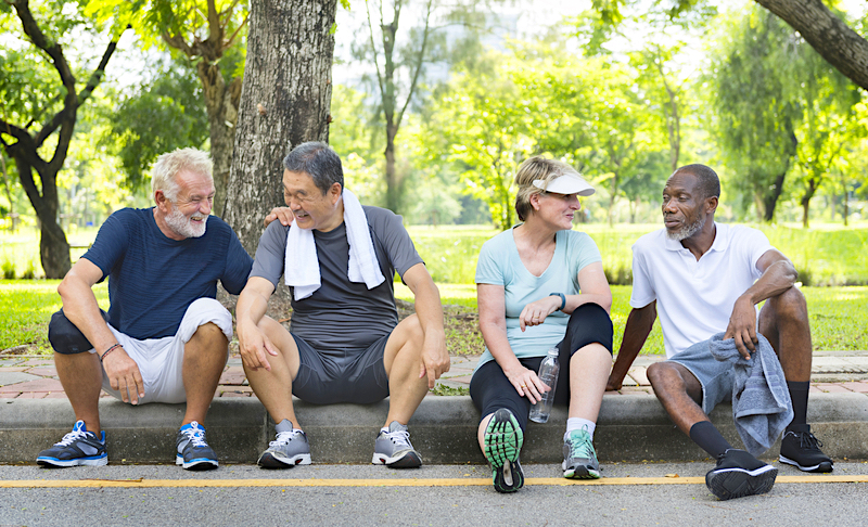 Four elderly or middle aged people sitting on a road curb talking to each other in exercise clothes