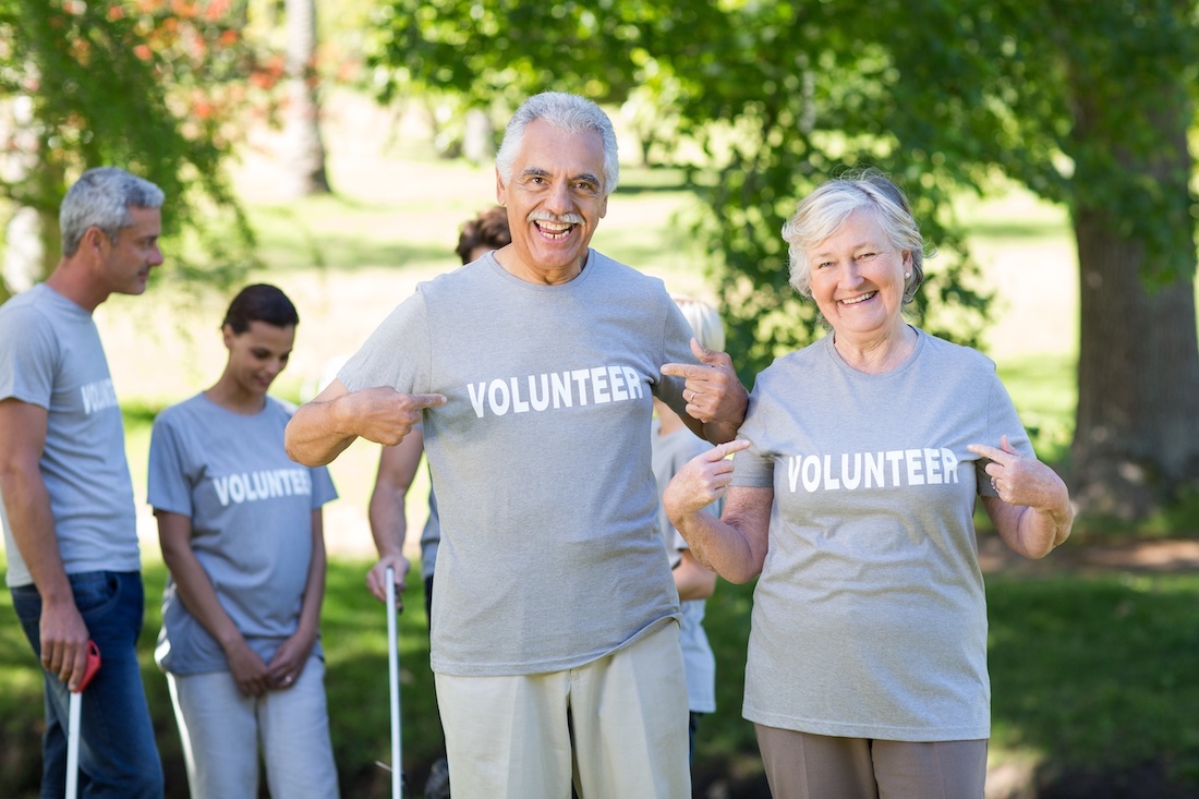 Elderly man and woman pointing to their shirts that say "Volunteer".
