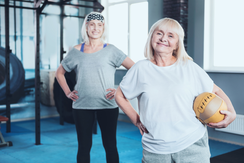 Two older women in a gym facing forward and smiling