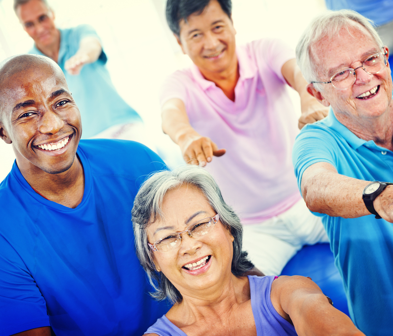 Group of older people, facing the camera and smiling, doing an arm exercise togther